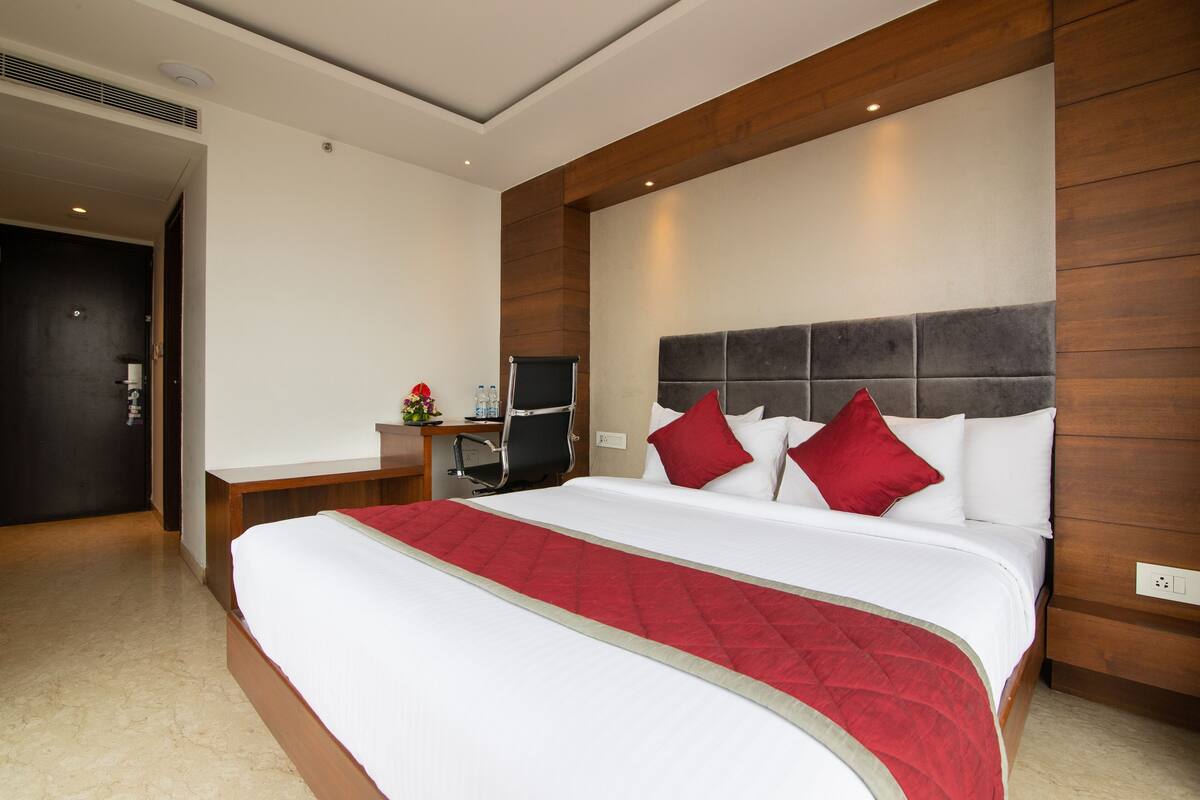 Habitación de hotel con una cama grande, cabecera de madera, escritorio con silla y una mesita con un jarrón de flores.