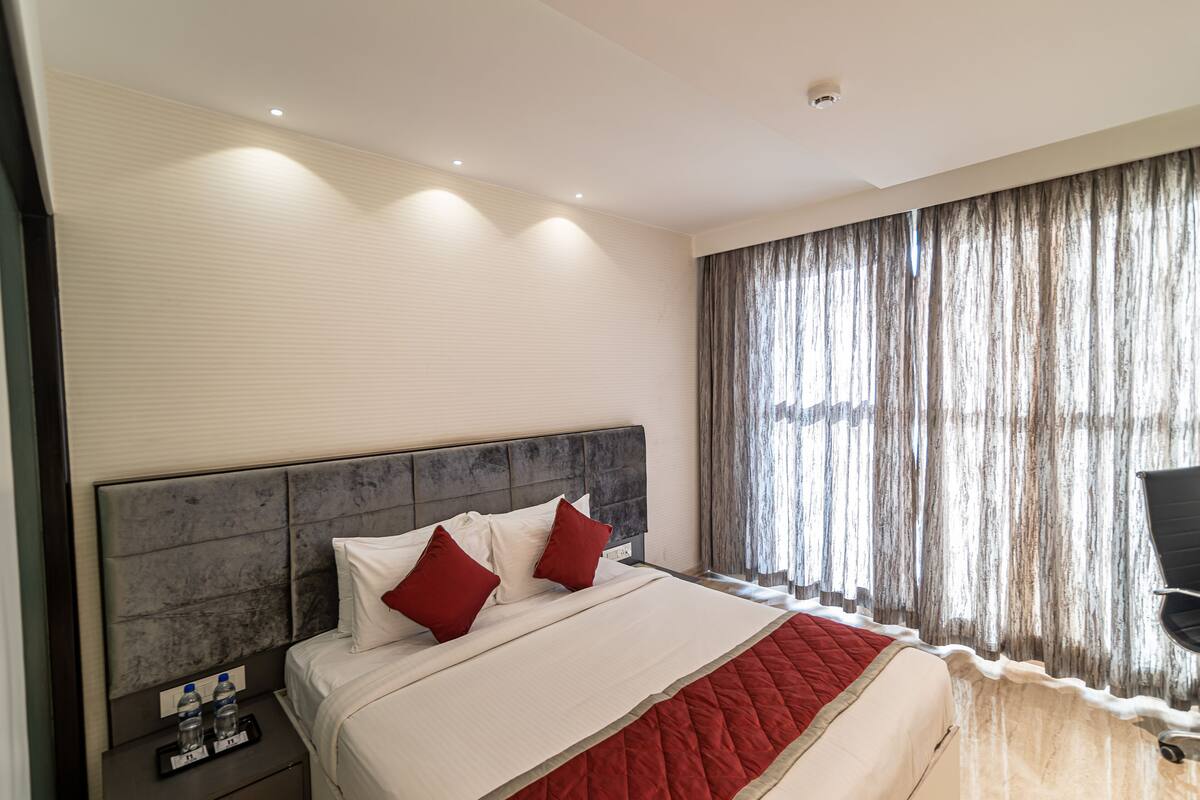 Una habitación de hotel con una cama grande, un cabecero, una mesita de noche con una bandeja y una ventana con cortinas.