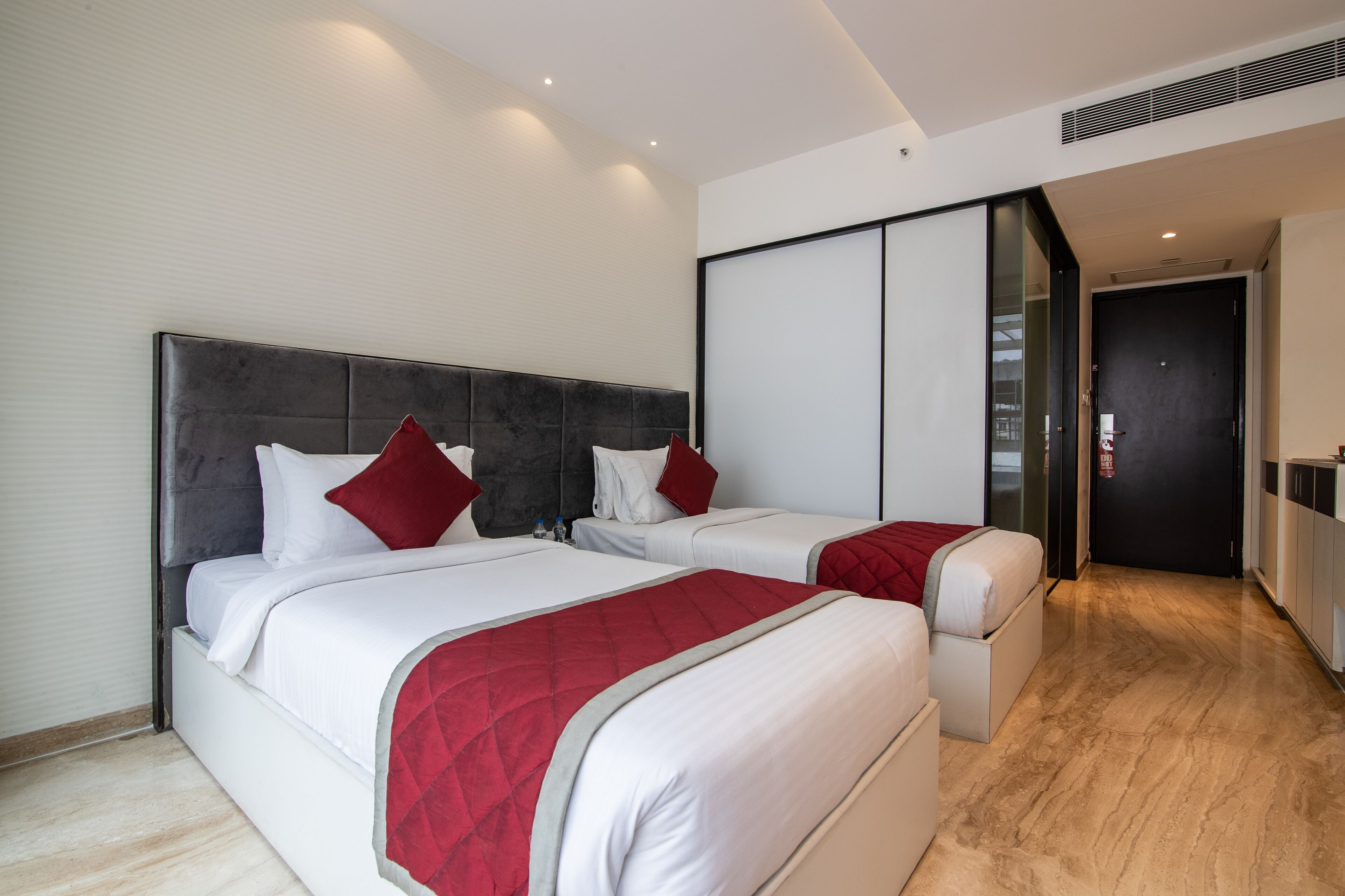A hotel room with two beds, a large sliding door, and a kitchenette.