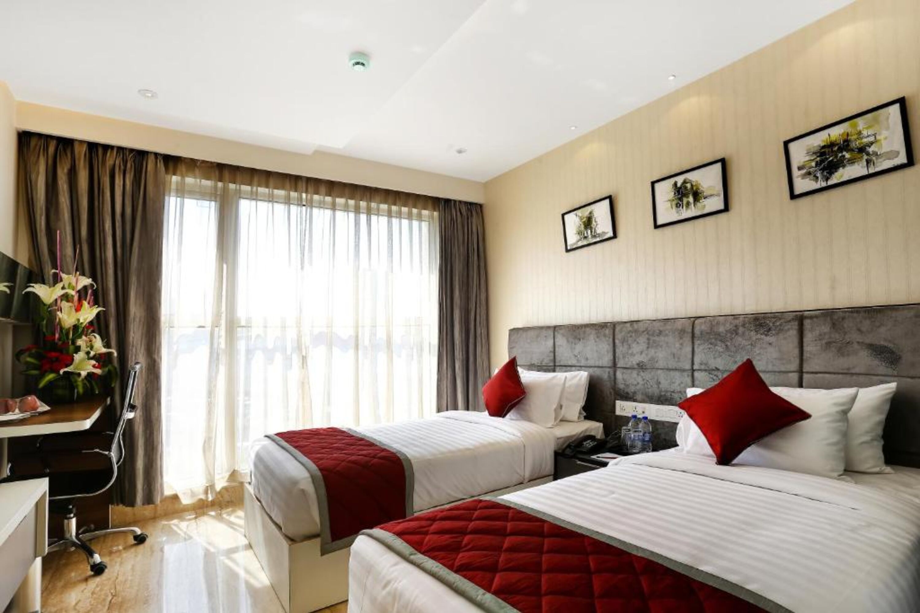 A hotel room with two beds, a desk, and a chair. There are curtains on the windows, and artwork on the walls.