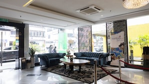 A hotel lobby with a reception desk, two blue sofas, a coffee table, a chandelier, and a large window with a view of the street. - Meritin Hotel (Kuching)