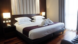A hotel room with a large bed, two bedside tables, a nightstand, a dark wooden floor, and a window with curtains. - Meritin Hotel (Kuching)