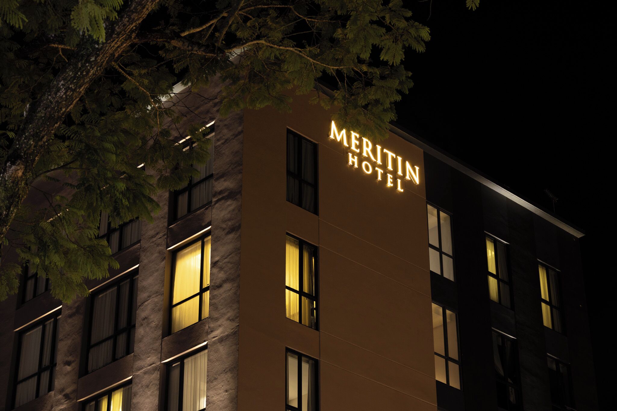 A hotel building with illuminated signage reading 'MERITIN HOTEL' at night.
