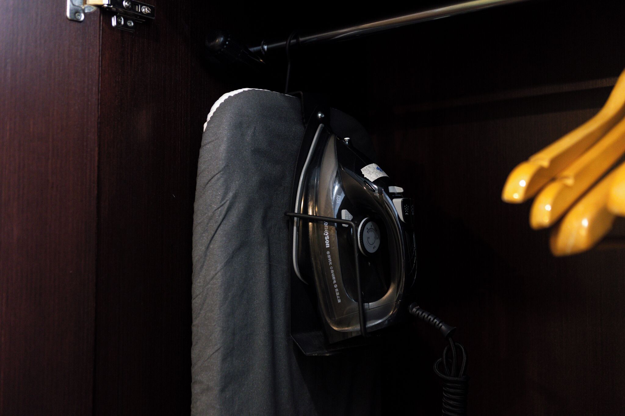 A compact, dark-colored closet with a hanging garment and a black iron appliance.