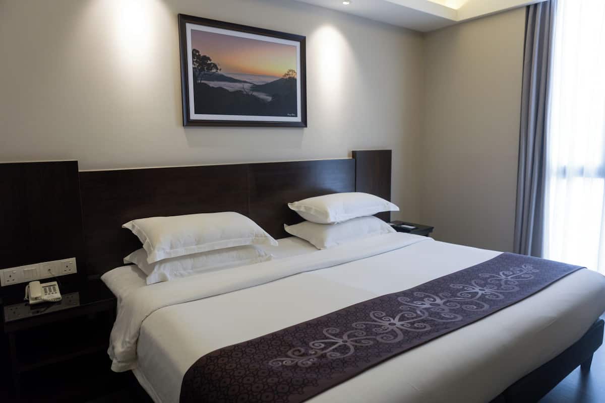 Una habitación de hotel con una cama grande, una mesita de noche con un teléfono y un cuadro enmarcado en la pared.