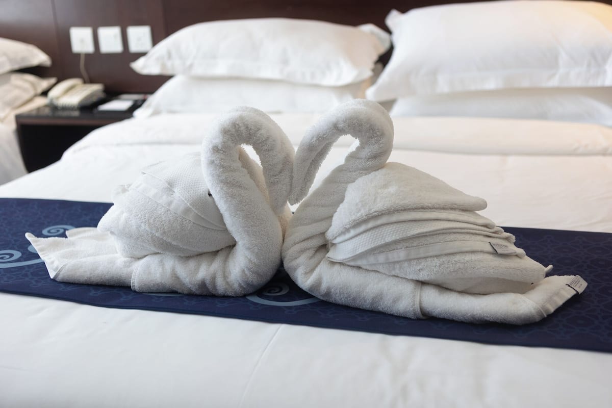 Una cama con almohadas blancas y una toalla doblada en forma de cisne.