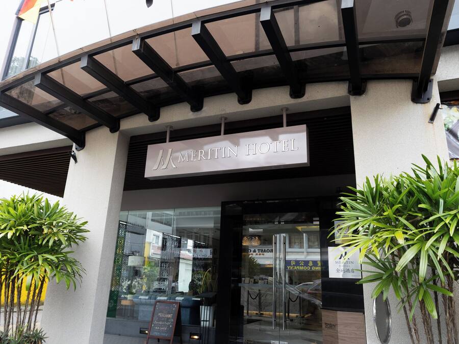 The exterior of the Meritin Hotel with a clear entrance, a covered walkway, and potted plants.