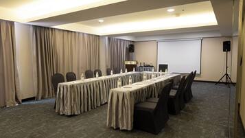 A conference room with a long table, chairs, a projector screen, and a speaker.