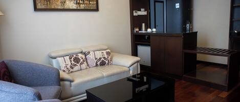A modern living room with a sofa, a coffee table, a painting, and a kitchenette area.