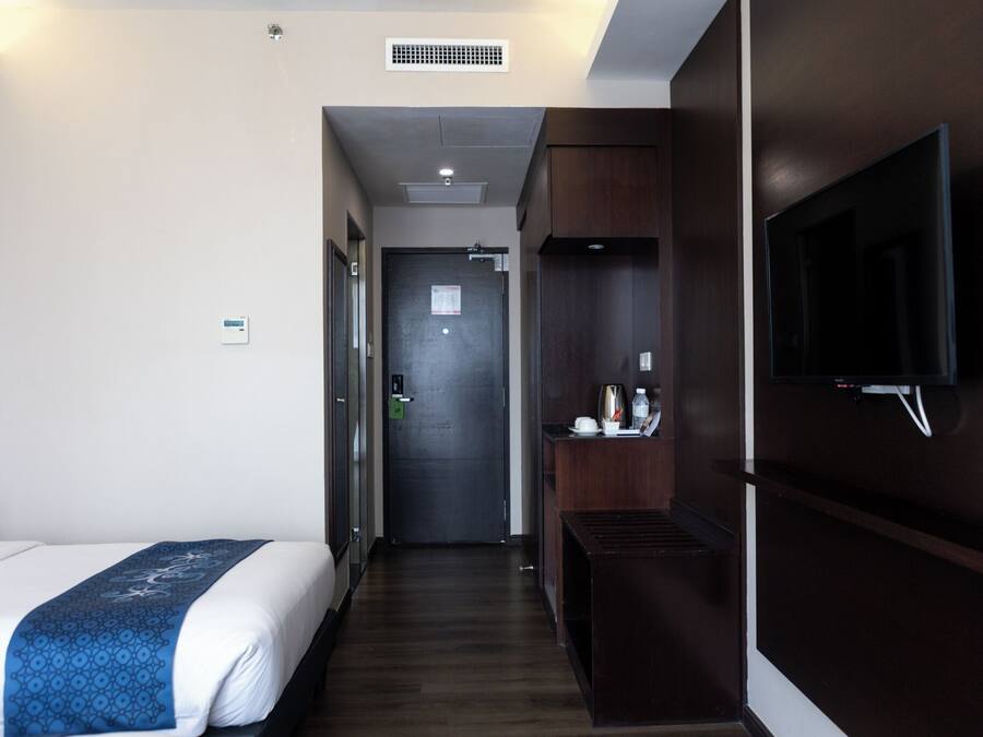 A hotel room with a bed, a TV mounted on the wall, a small table with a kettle, and a door leading to another room.
