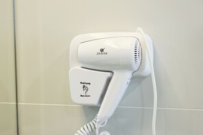 A wall-mounted hair dryer with a cord, attached to a tiled wall. - Meritin Hotel (Kuching)