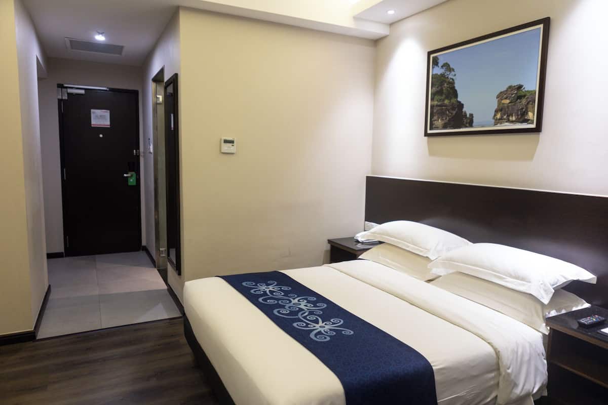 Habitación de hotel con cama, mesita de noche, un cuadro en la pared y una puerta al fondo.