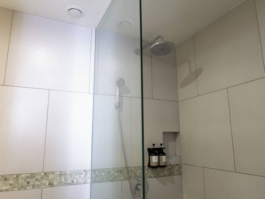 Eine Duschkabine mit Handbrause, am Wand montiertem Wasserhahn und Wandseifenspender.