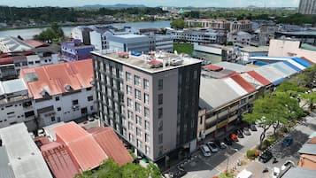 Ein mehrstöckiges Hotel mit flachem Dach, umgeben von anderen Gebäuden und einem Fluss.