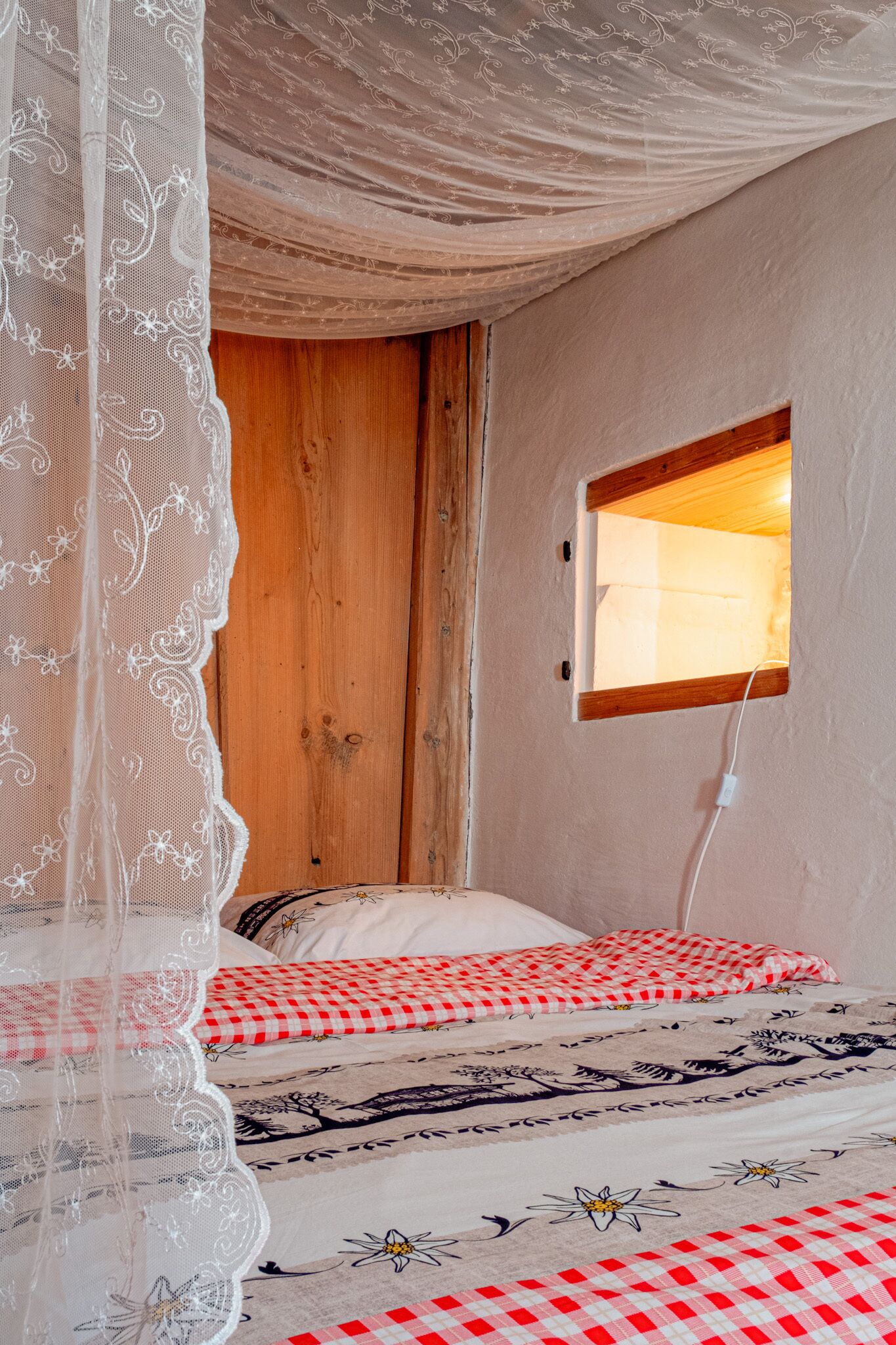 Ein Schlafzimmer mit Holztür, einem Fenster mit Holzrahmen und einem Bett mit karierter Bettwäsche.