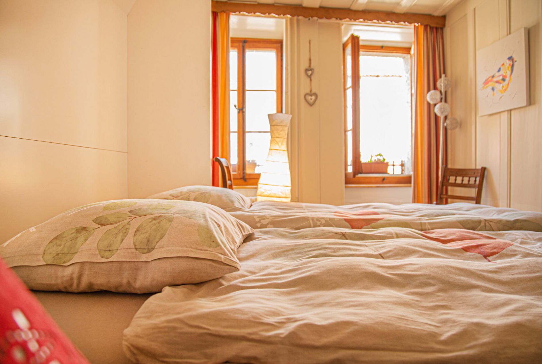Ein Schlafzimmer mit einem Bett, zwei Stühlen, einem fensterbelaubten Fenster und einer Wandlampe.