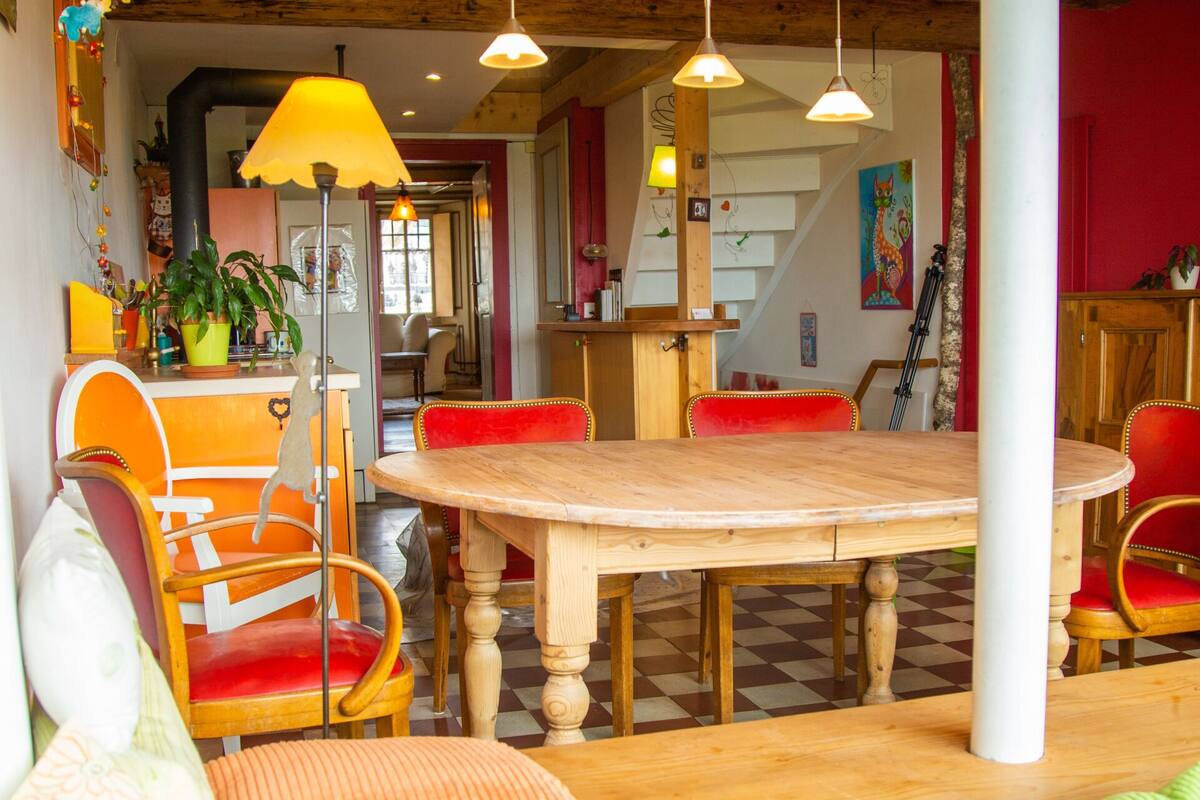 Ein gemütlicher Essbereich mit Holztisch und -stühlen, einer Hängelampe und einer farbenfrohen Wanddekoration.