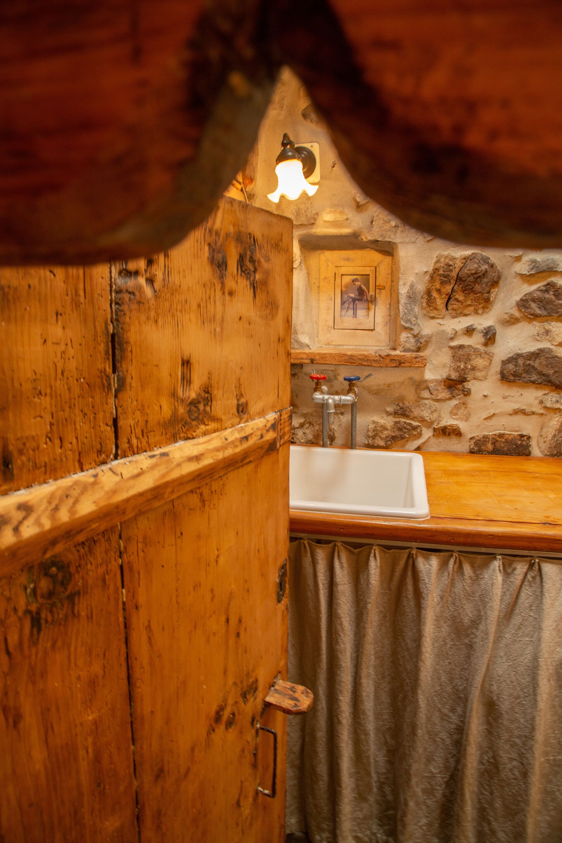 Un baño rústico con puerta de madera, pared de piedra y un lavabo.