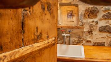 Un baño rústico con puerta de madera, pared de piedra y un lavabo.
