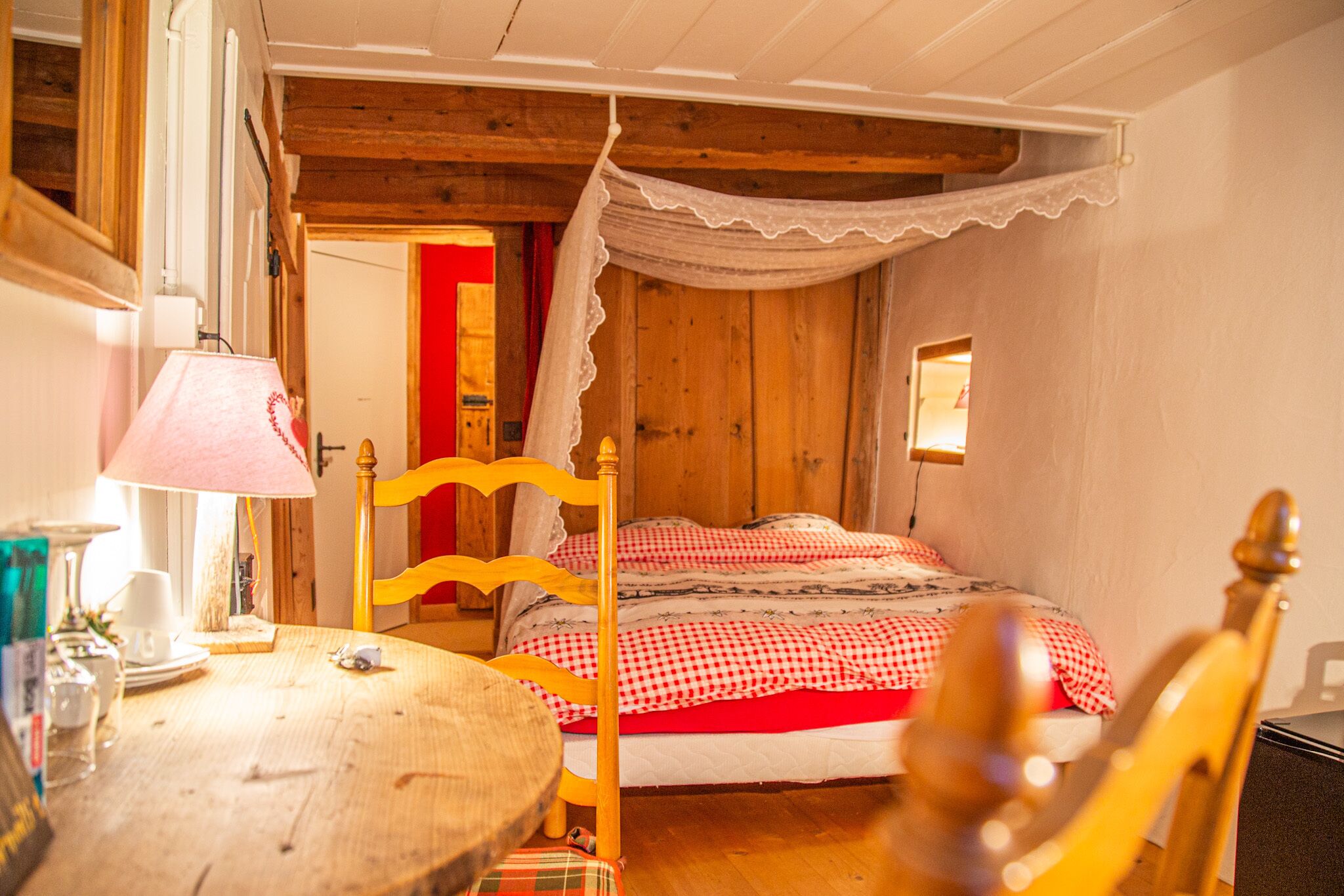 Um quarto acolhedor com uma cama de madeira, uma mesa redonda pequena com uma luminária e uma cadeira.