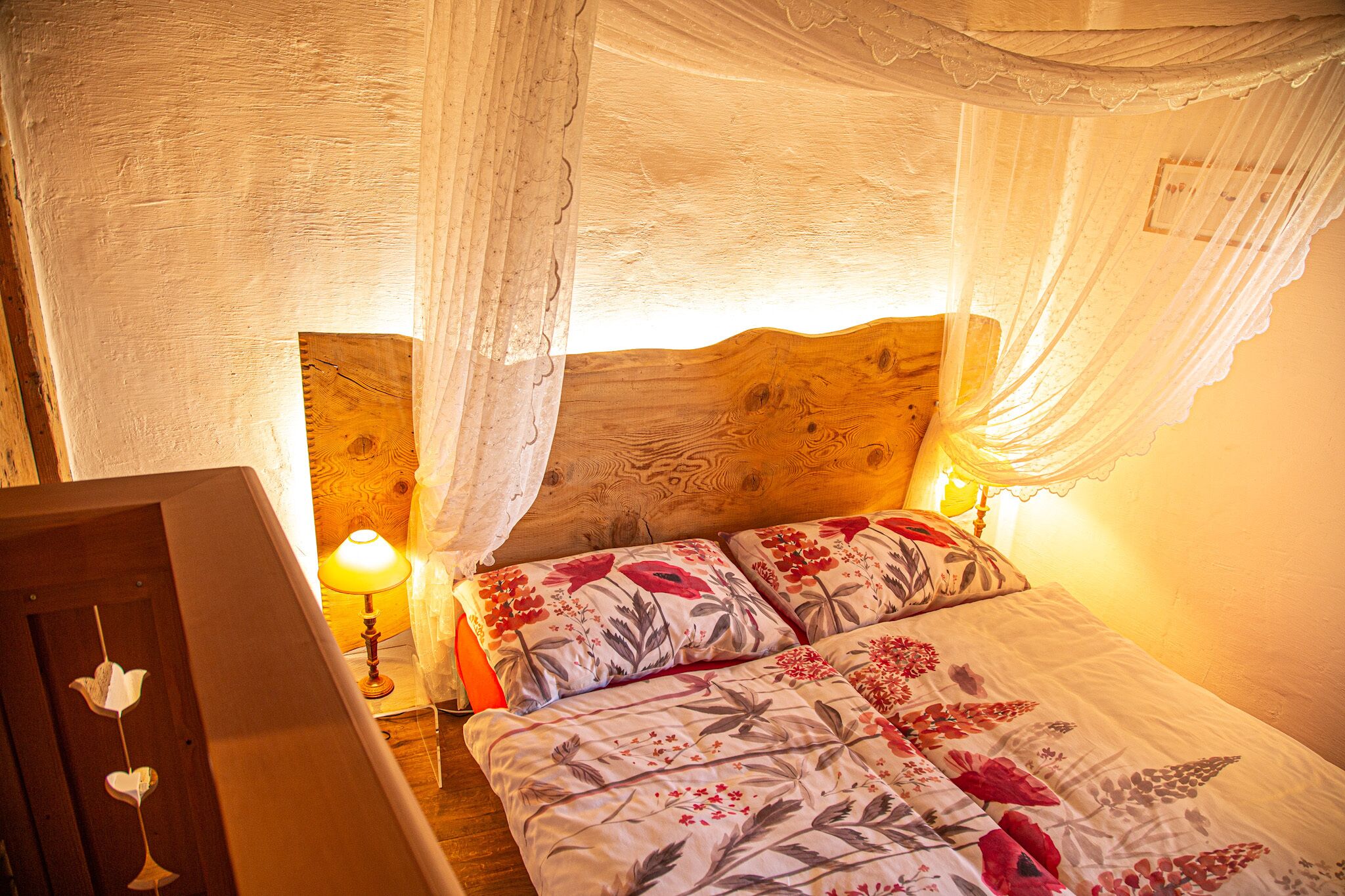 Een slaapkamer met een houten hoofdbord, bloemenbeddengoed, een bedlampje en een nachtkastje.