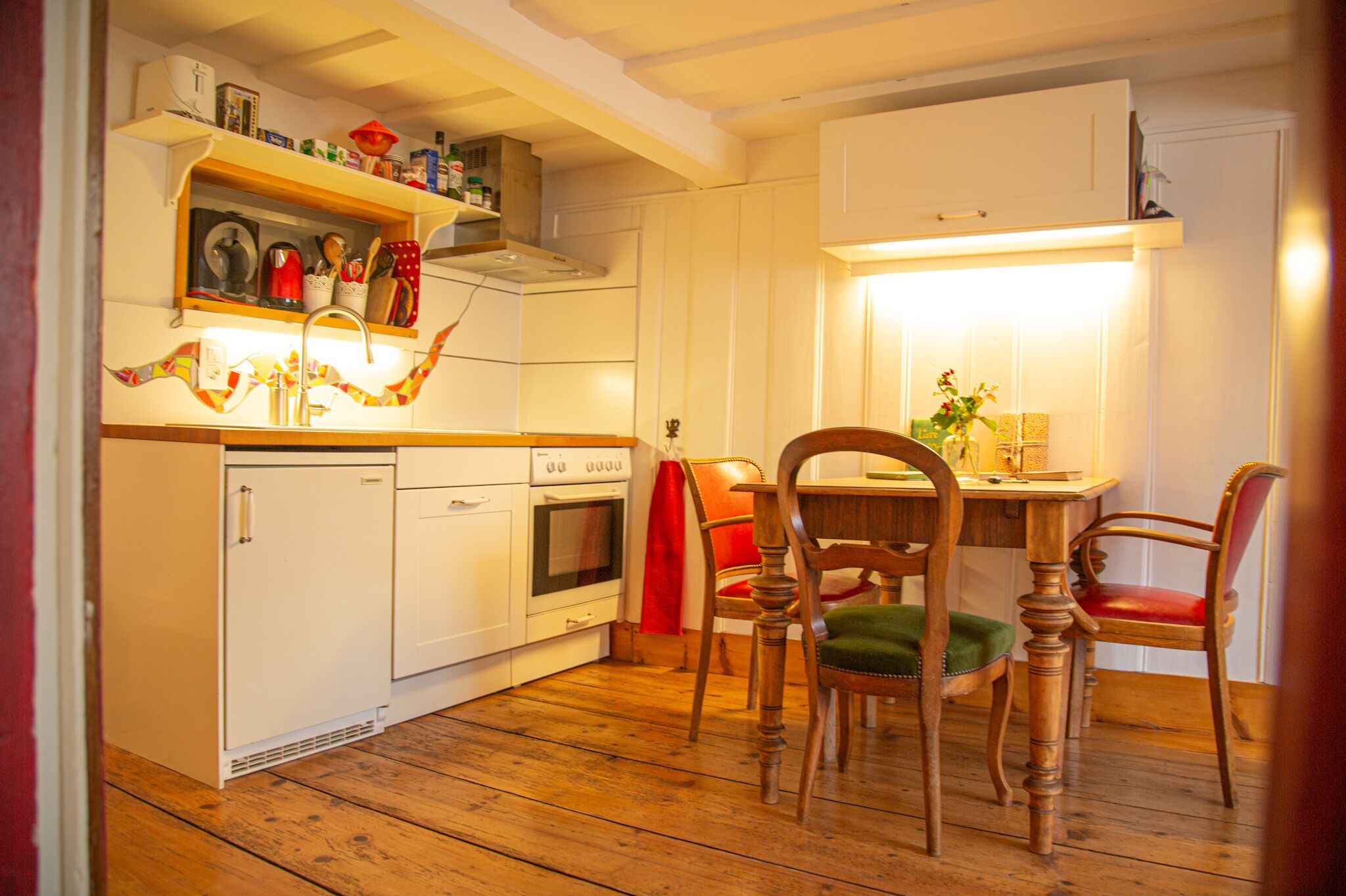 A kitchen with wooden flooring, white cabinets, a dining table with chairs, and a red towel on the chair.