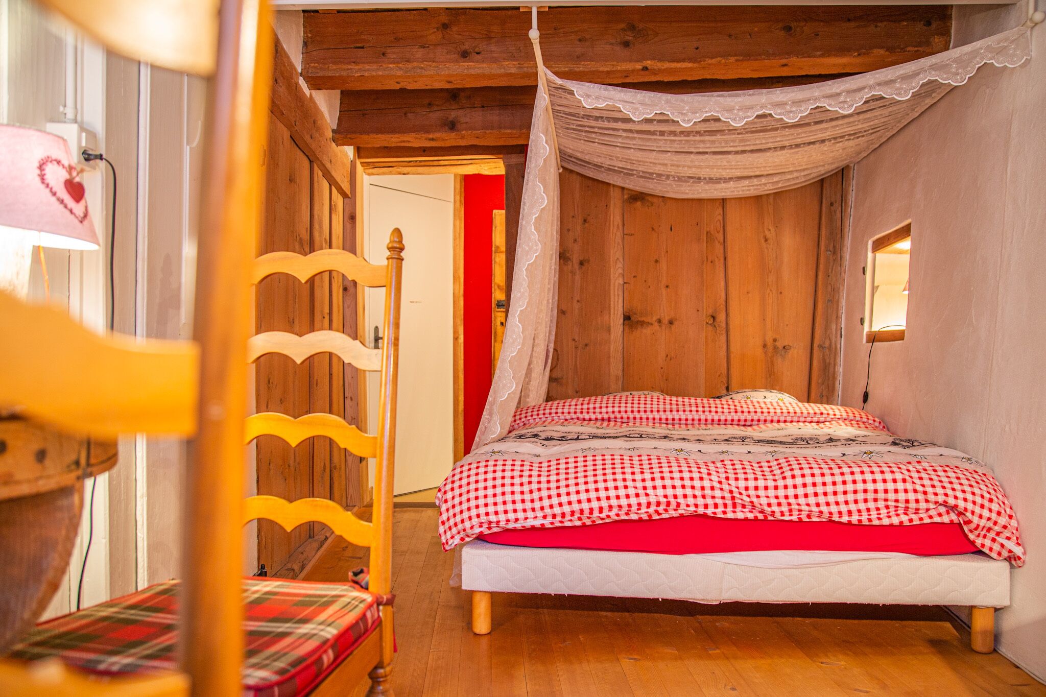 A wooden room with a bed, a chair, and a window.