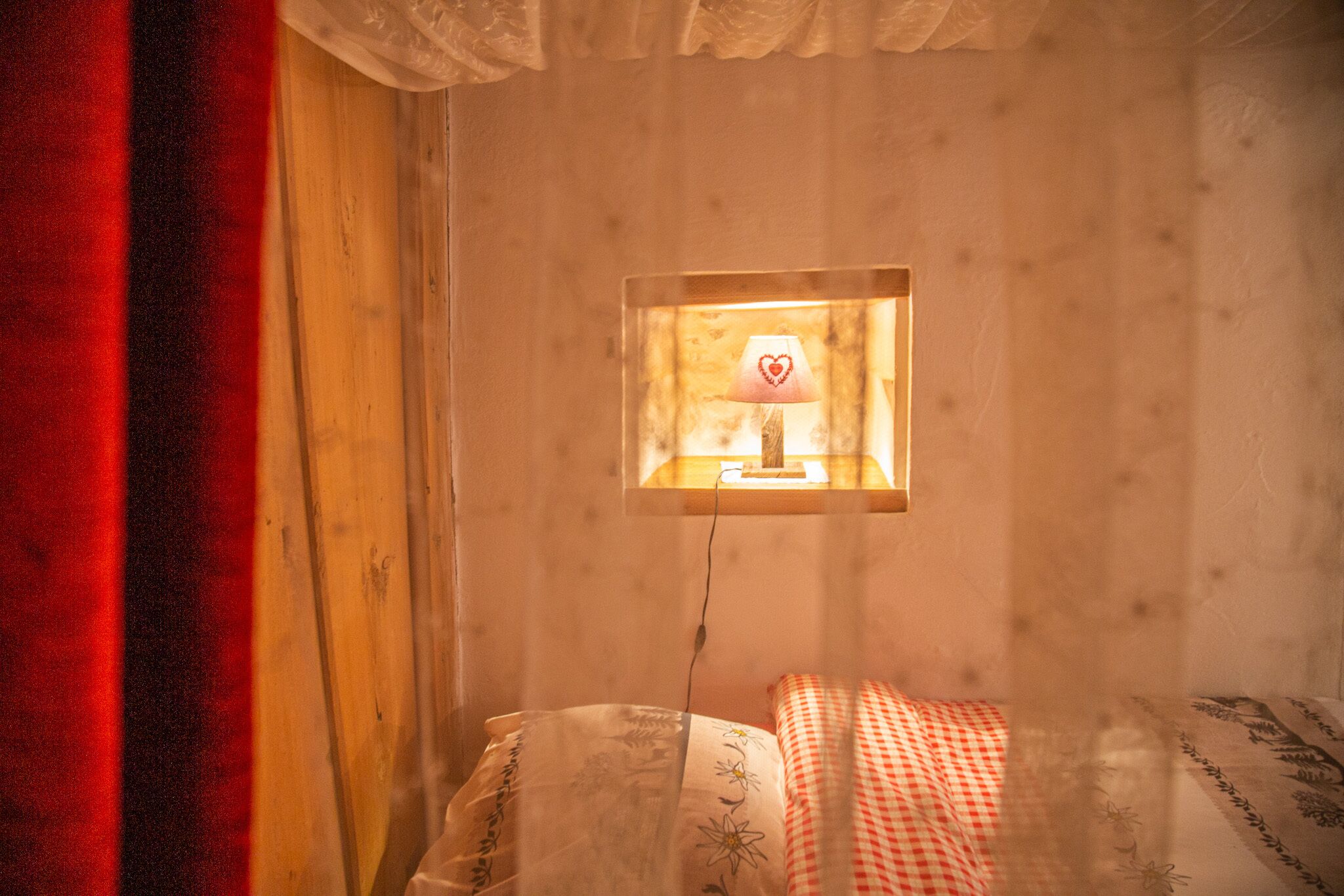 A bedroom with a bed, a bedside table with a lamp, and a window with curtains.