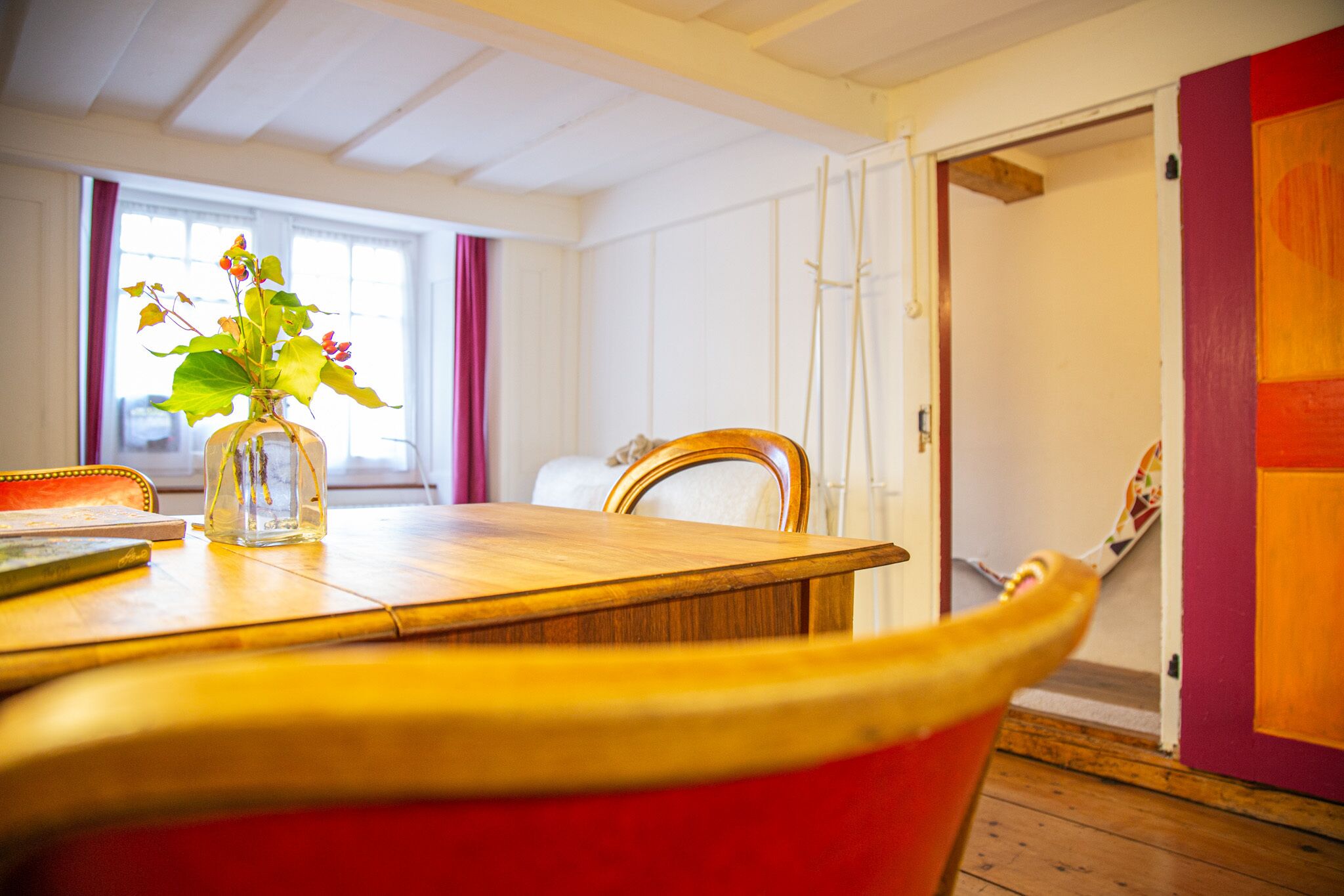 Een eetgedeelte met een houten tafel, een vaas met bloemen en een rode stoel.