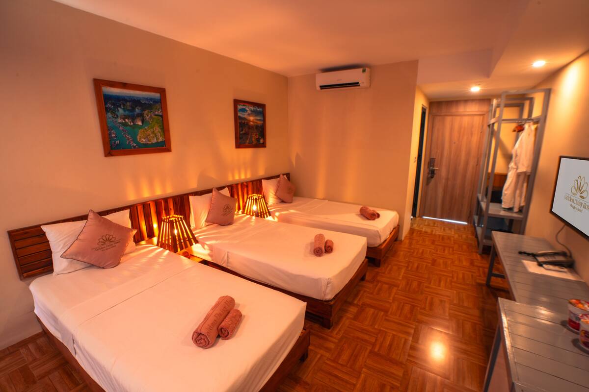 A hotel room with three beds, wooden flooring, and a TV on a desk.