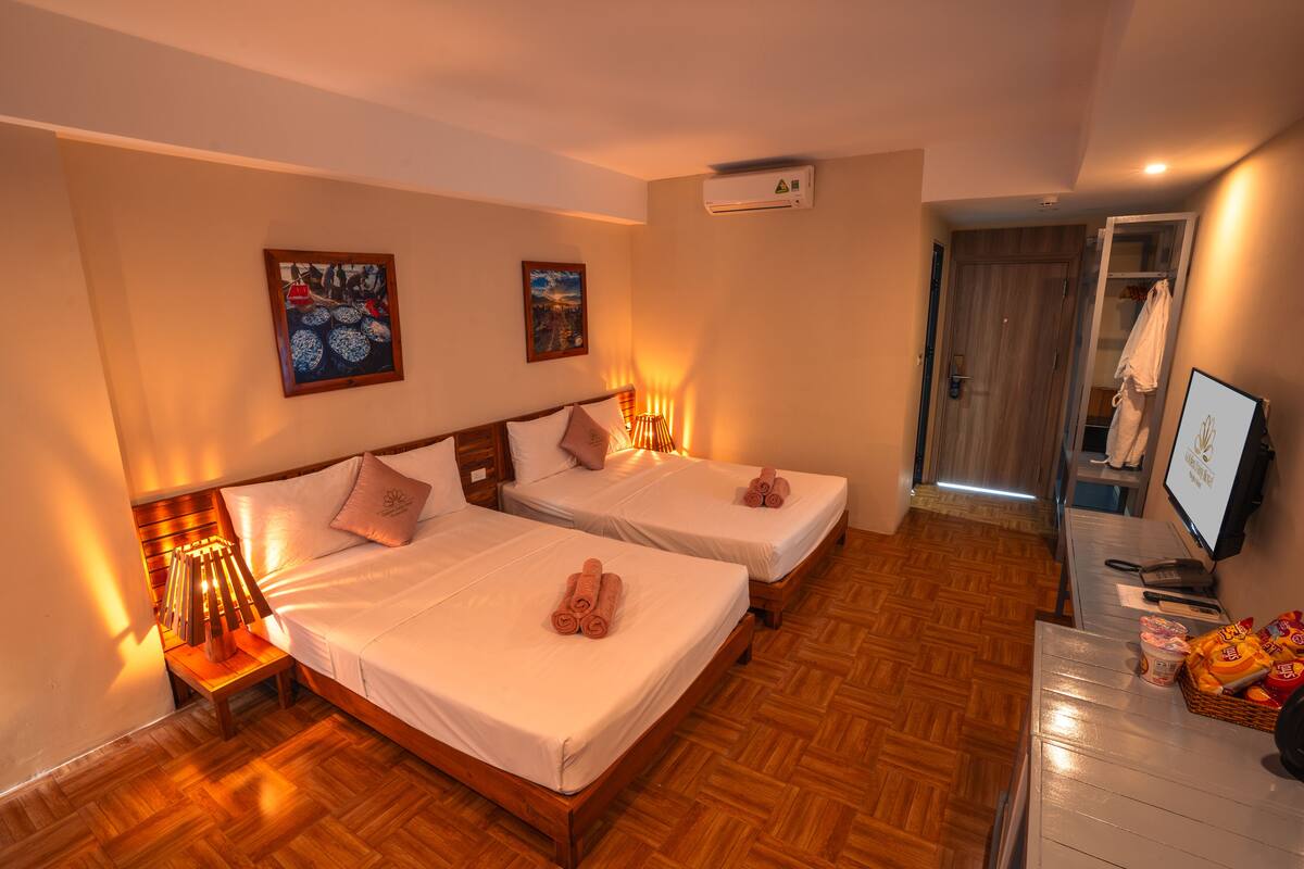 A hotel room with two beds, wooden flooring, and a small desk with a basket of snacks.