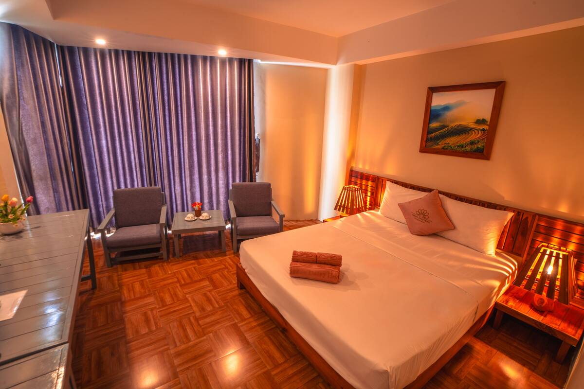 A hotel room with a large bed, two armchairs, a small table, and a painting on the wall.