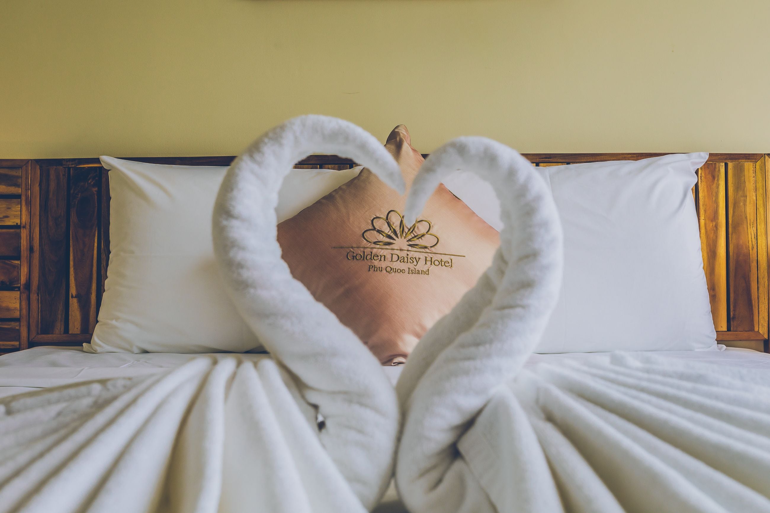 Una cama con ropa de cama blanca y una almohada con el logotipo del Hotel Golden Daisy.
