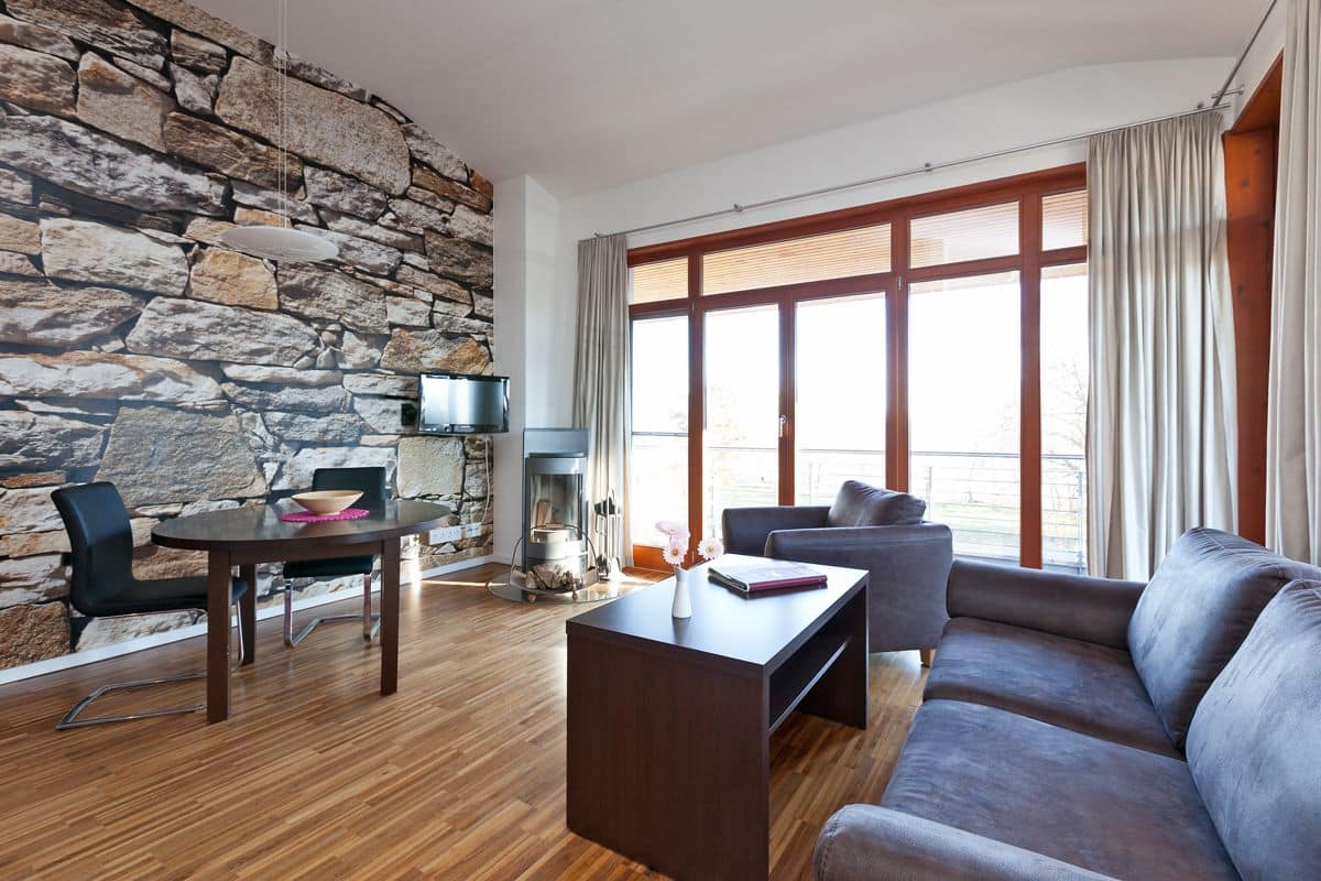 A modern living room with a stone wall, wooden flooring, a sofa, a coffee table, a TV, and a fireplace.