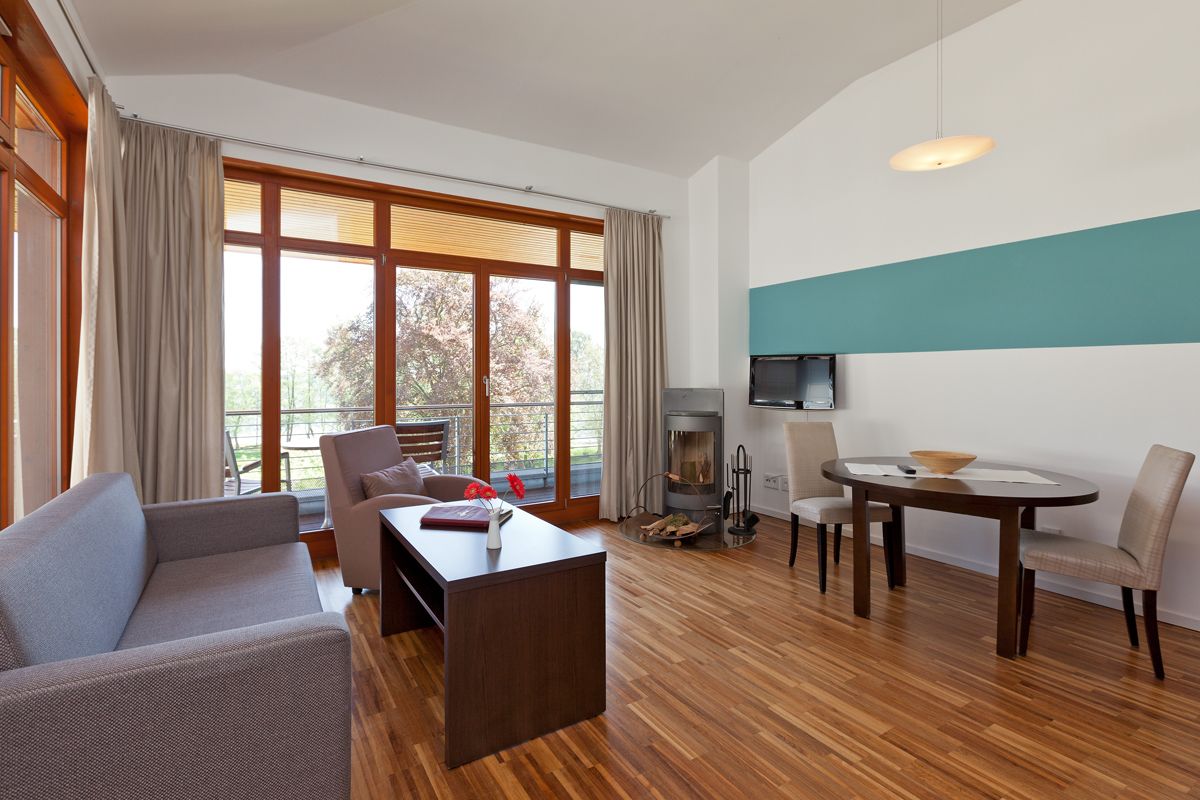 A modern living room with a sofa, a coffee table, a dining table with chairs, a fireplace, and large windows with curtains.