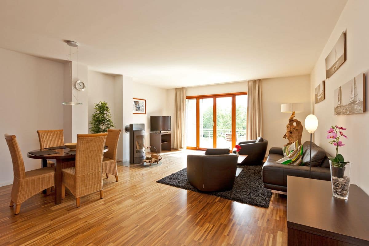 A modern living room with a dining area, a fireplace, and a large window offering a view of greenery.