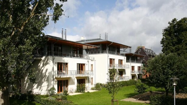A modern multi-story building with balconies, a well-maintained garden, and a clear sky. - Seeresidenz Klink (Klink)