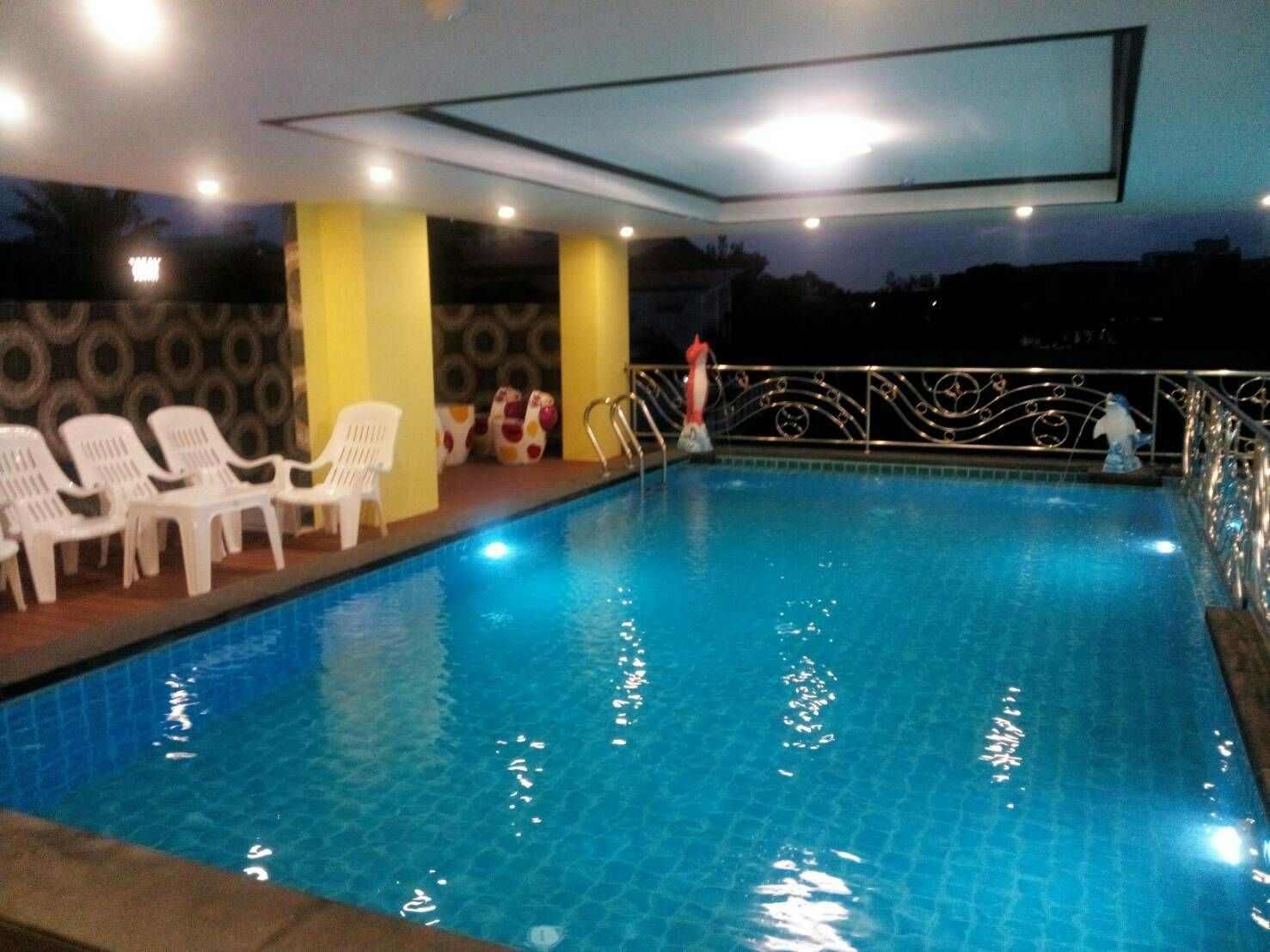 An indoor swimming pool with clear blue water, surrounded by white lounge chairs and a decorative railing.