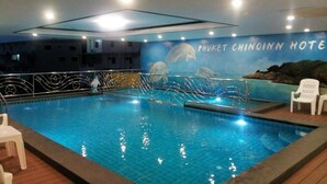 Une piscine intérieure ornée d’une fresque représentant des dauphins et d’un panneau indiquant : « HÔTEL PHUKET CHINOINN ».