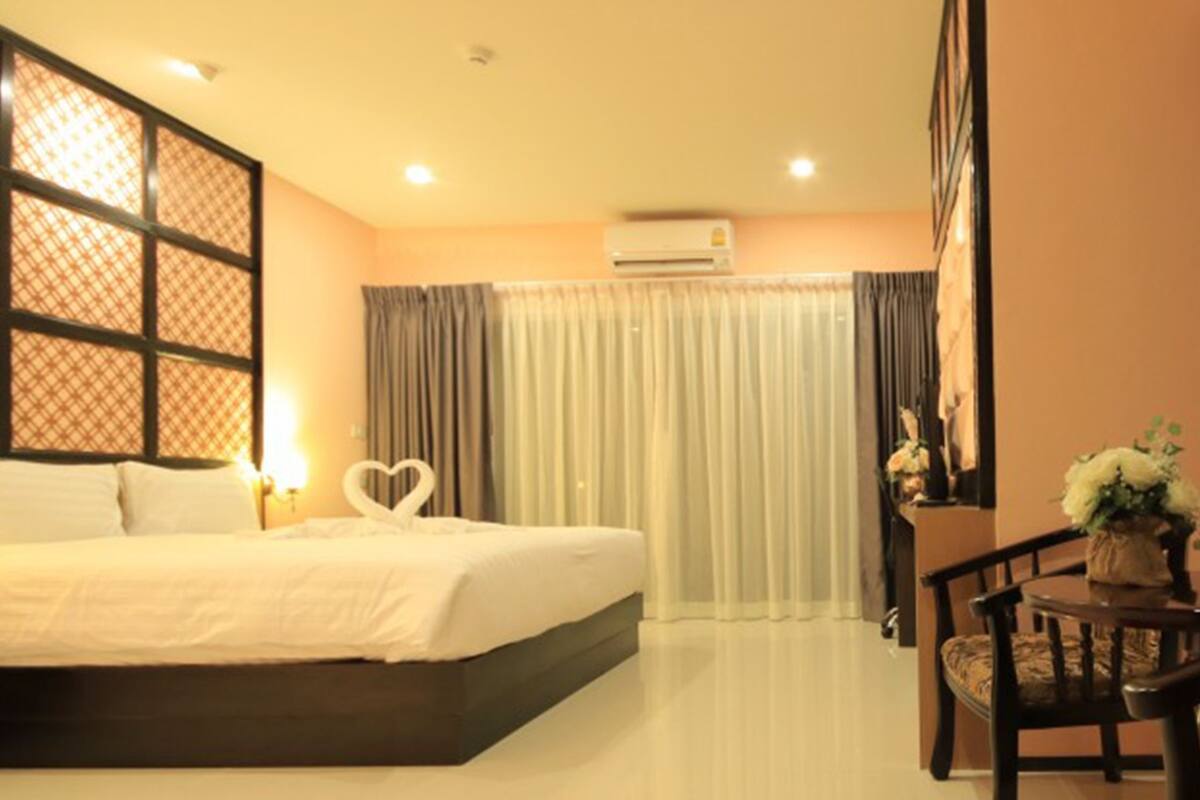 A hotel room with a bed, a desk with a chair, a window with curtains, and an air conditioning unit.