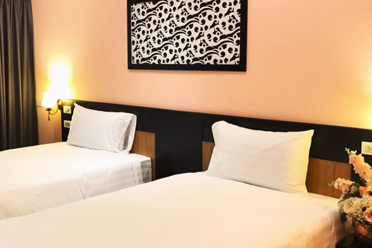 A hotel room with two beds, a decorative wall piece, a nightstand with a lamp, and a floral arrangement.