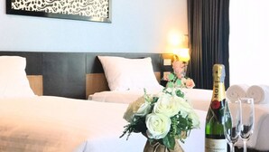 Une chambre d’hôtel avec un lit, une table de chevet sur laquelle se trouve une bouteille de champagne et deux verres, ainsi qu’un bouquet de fleurs.