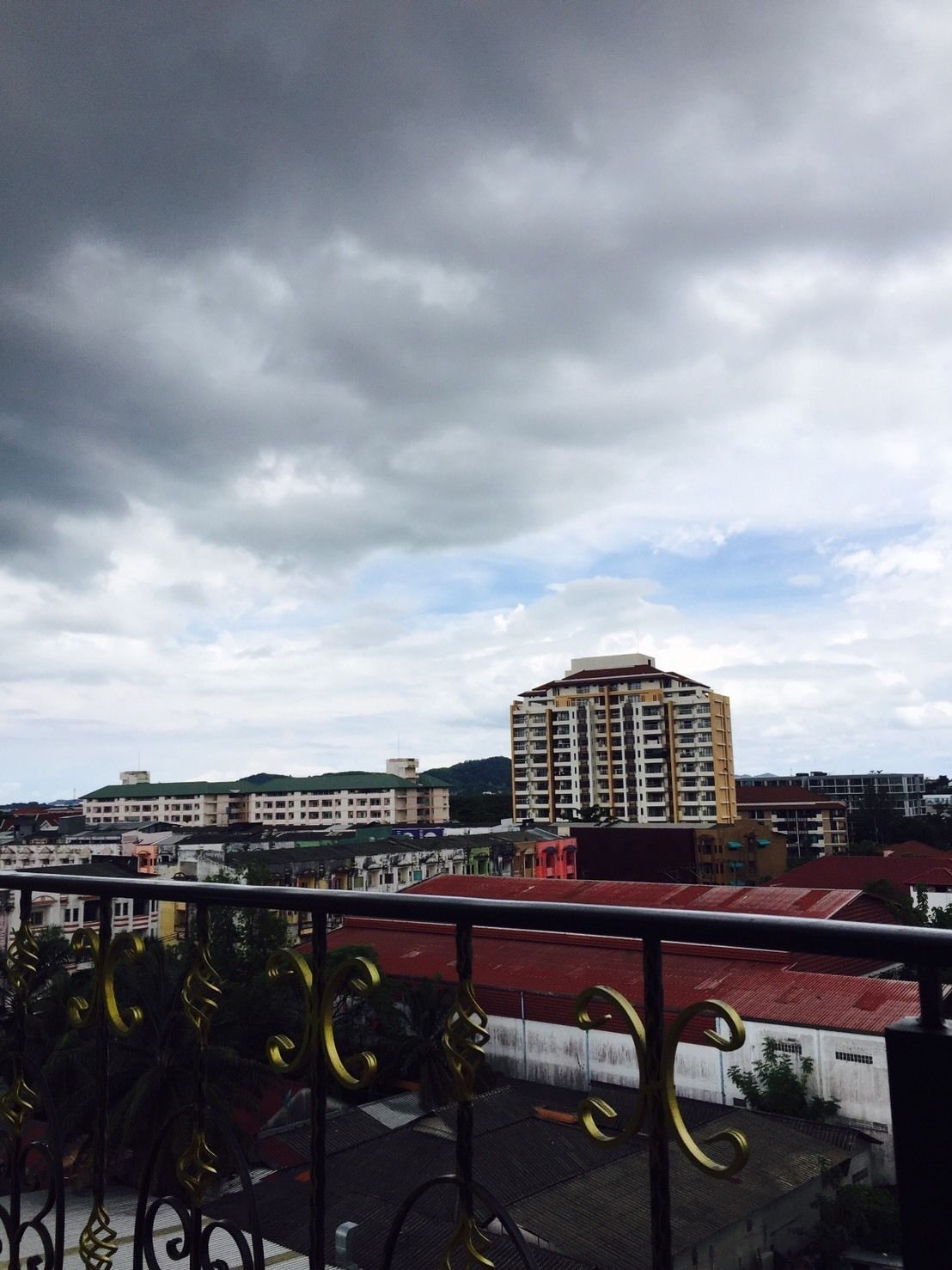 A cityscape with a prominent multi-story building in the center, surrounded by other buildings and a cloudy sky.