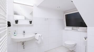 A modern bathroom with a white sink, mirror, and toilet. There is a towel rack and a window above the toilet.