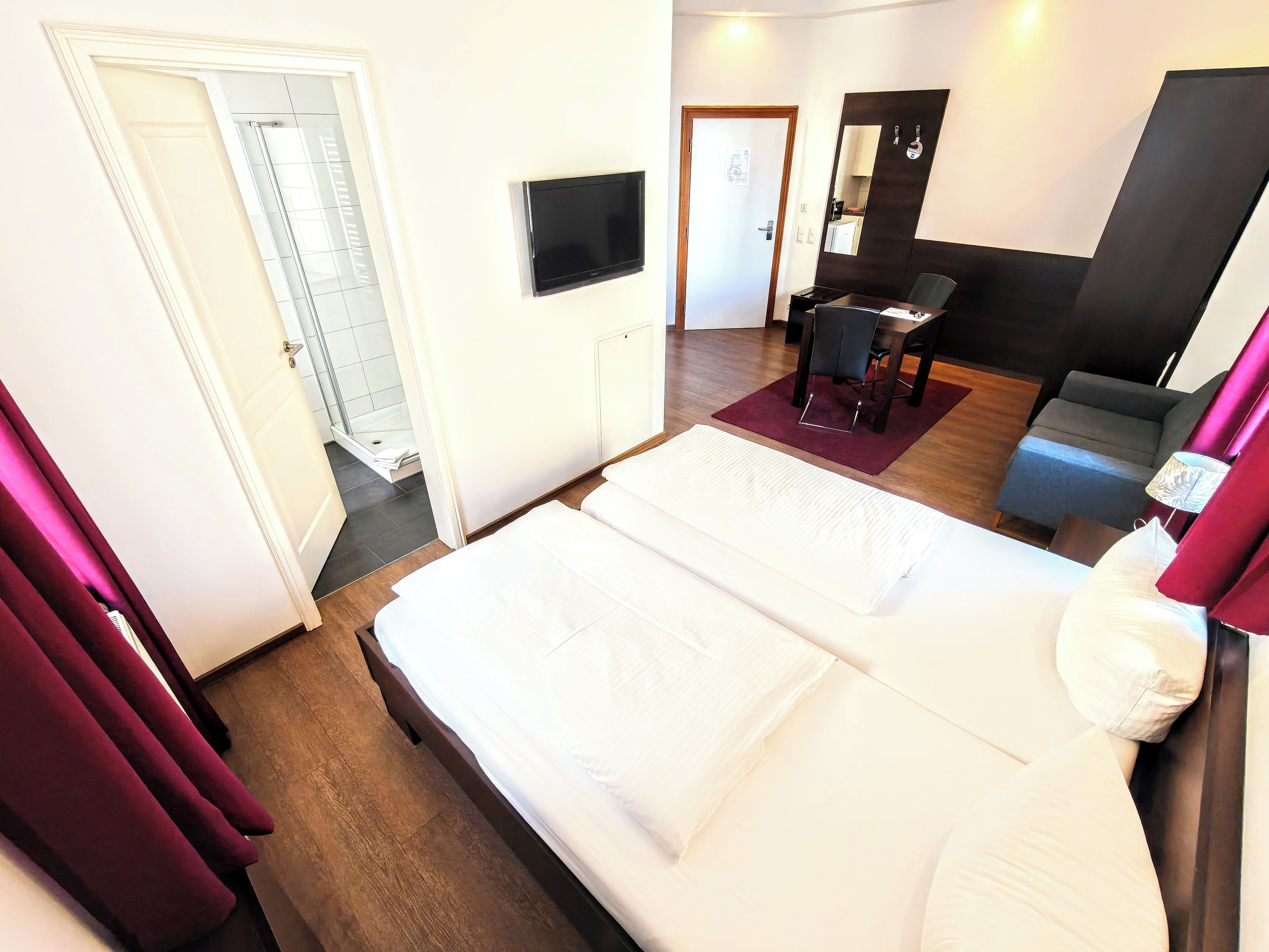 A hotel room with two beds, a TV, a desk, a chair, and a mirror.