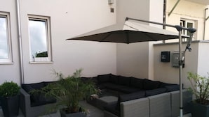 Ein moderner Außenbereich mit einer Eckcouch, Pflanzkübeln und einem großen Sonnenschirm.