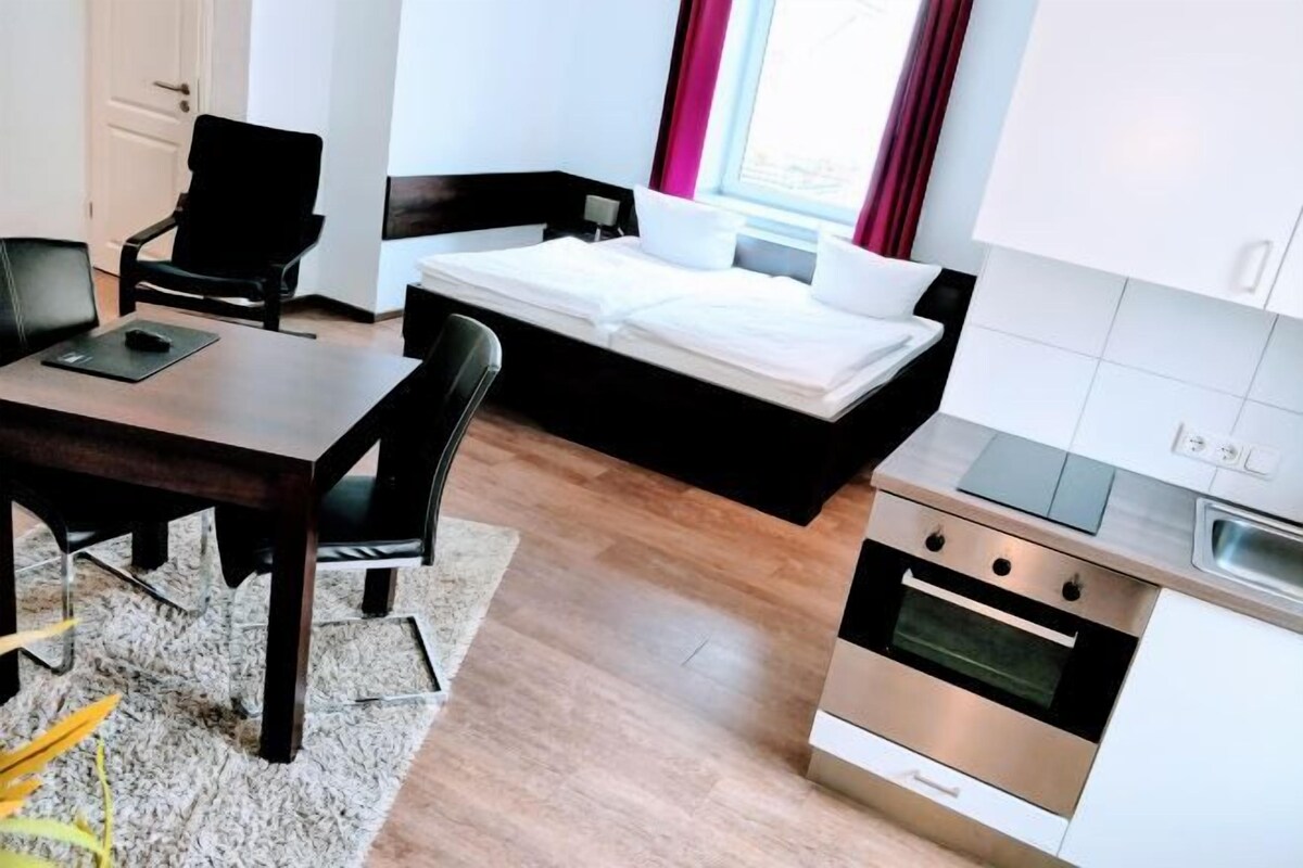 Een compacte kamer met een bed, een kitchenette, een eettafel en een stoel.