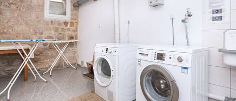 A laundry area with two washing machines, a drying rack, and a stone wall.