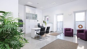 Ein moderner Arbeitsraum mit weißen Schränken, einem Schreibtisch, zwei schwarzen Stühlen, einem violetten Sofa und einer Topfpflanze.