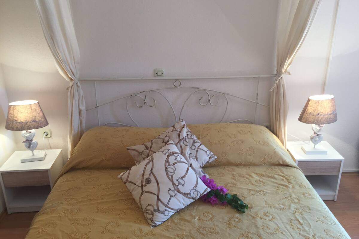 Una cama con un edredón estampado, dos lámparas de noche y un cojín decorativo.
